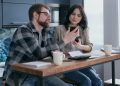 a couple sitting near the wooden table while holding mobile phones