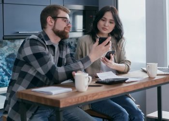 a couple sitting near the wooden table while holding mobile phones
