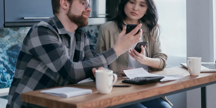a couple sitting near the wooden table while holding mobile phones