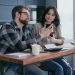 a couple sitting near the wooden table while holding mobile phones