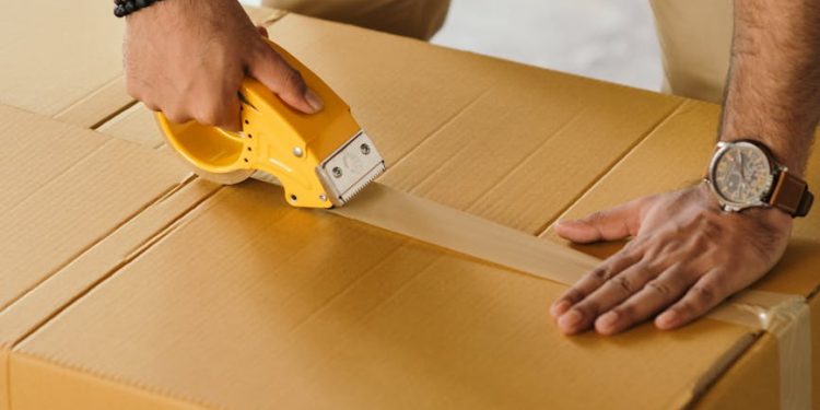 crop man sealing box with scotch tape